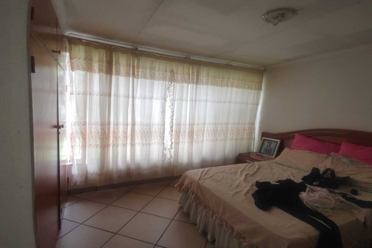 A bedroom featuring tiled flooring, built-in cabinetry, and large windows with curtains, offering a functional space with potential for modernization.