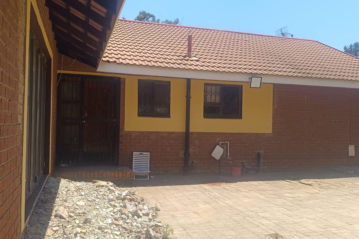 Rear exterior view of the house featuring a paved courtyard, brick facade, and tiled roof with security gates on the entrance.