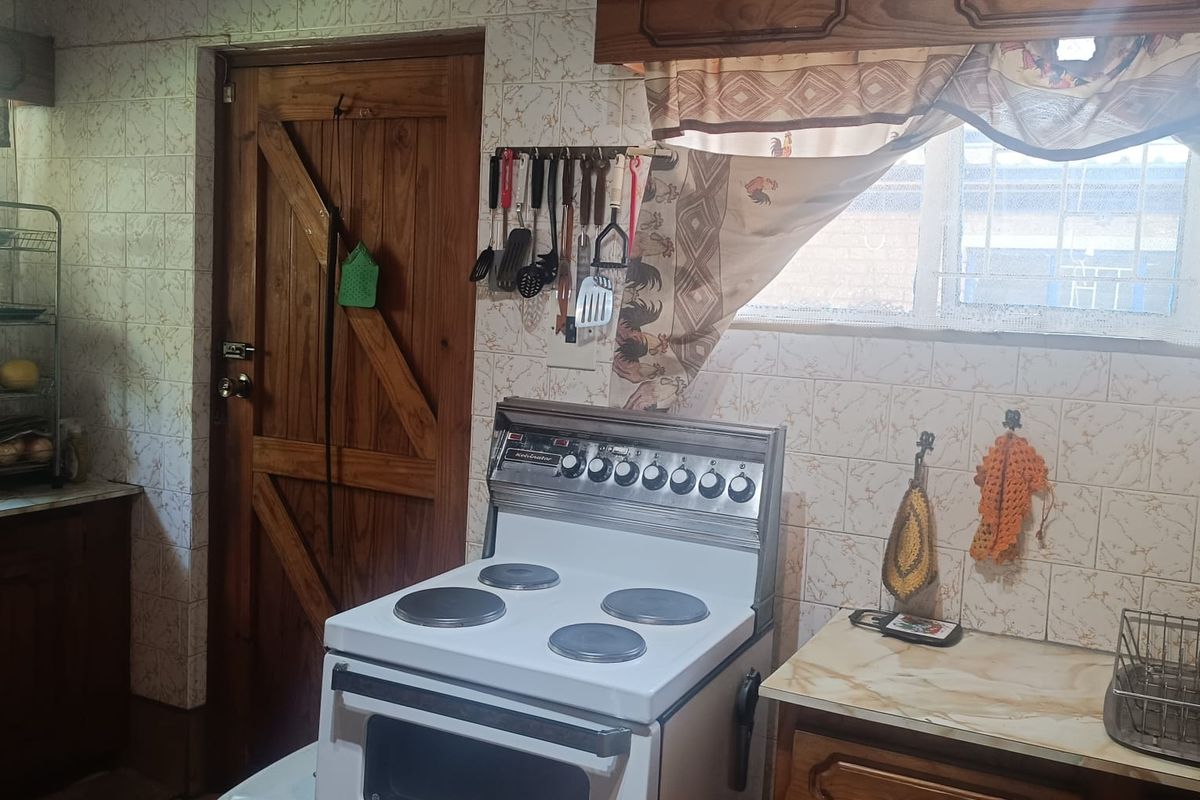 A dated kitchen featuring traditional wooden cabinetry, tiled walls, and a freestanding electric stove, offering a functional layout with potential for modernization.