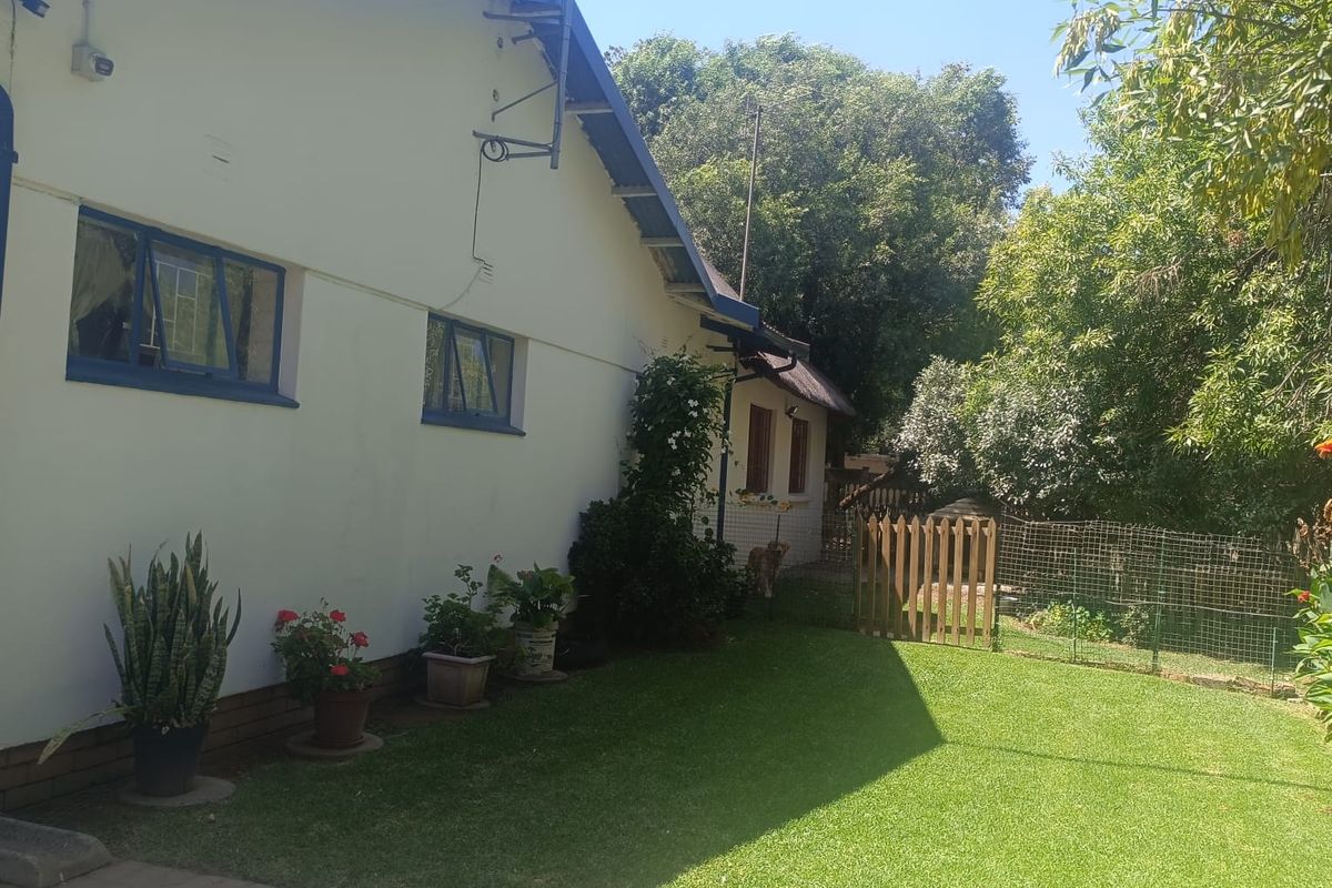A view of the rear exterior of the house featuring a well-maintained lawn, paved area, and perimeter fencing.