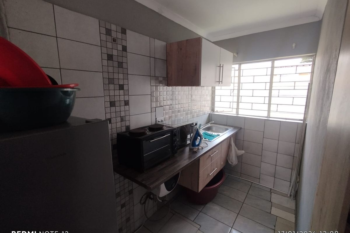 Compact kitchen area featuring built-in cabinetry, a stainless steel sink, and tiled wall finishes with a window providing natural light.