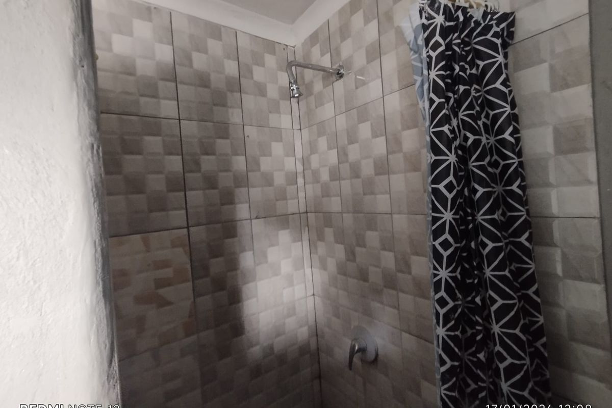 A functional shower area featuring full-height wall tiling, a wall-mounted shower head, and a single-lever mixer tap.