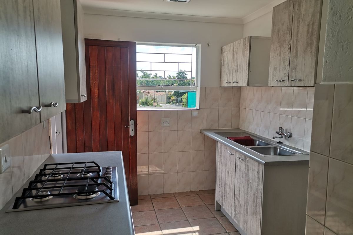 Functional kitchen featuring wood-look cabinetry, a built-in gas hob, double stainless steel sink, and tiled splashbacks with direct access to the exterior.