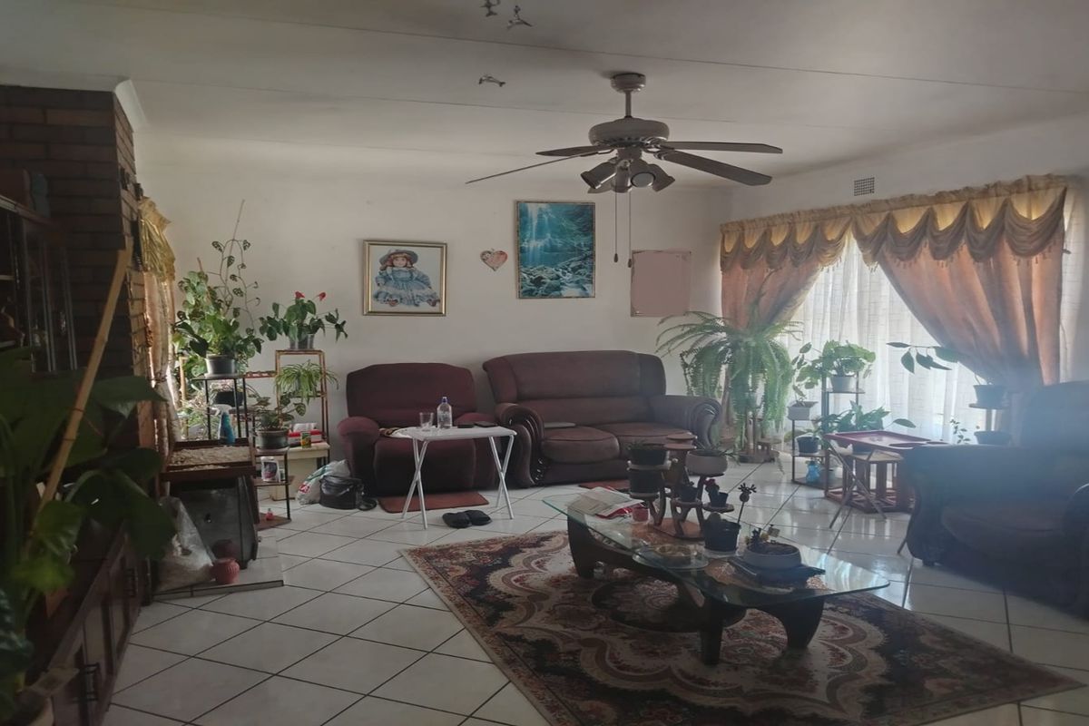 Spacious living room featuring tiled flooring, a ceiling fan, and a brick fireplace surround, offering a comfortable and traditional living space.