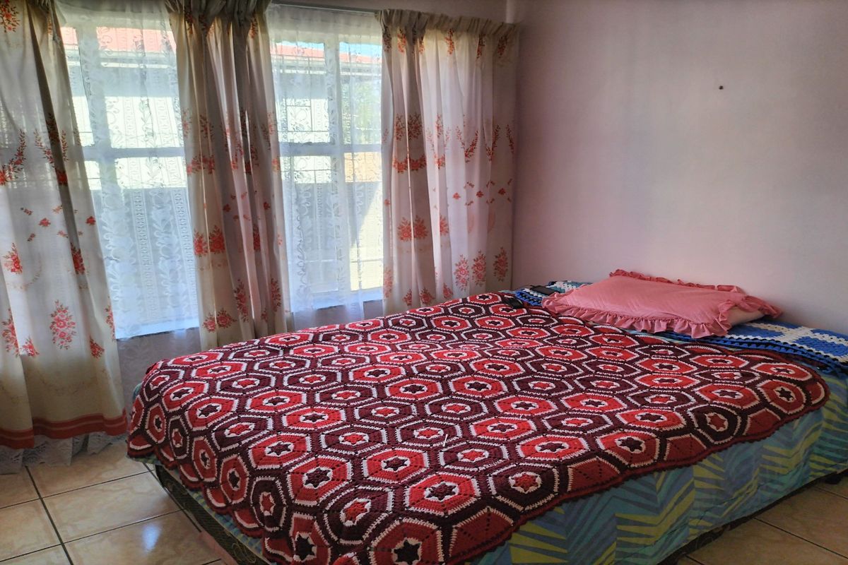 A bedroom featuring tiled flooring and large windows with curtains, providing natural light and a view of the exterior.