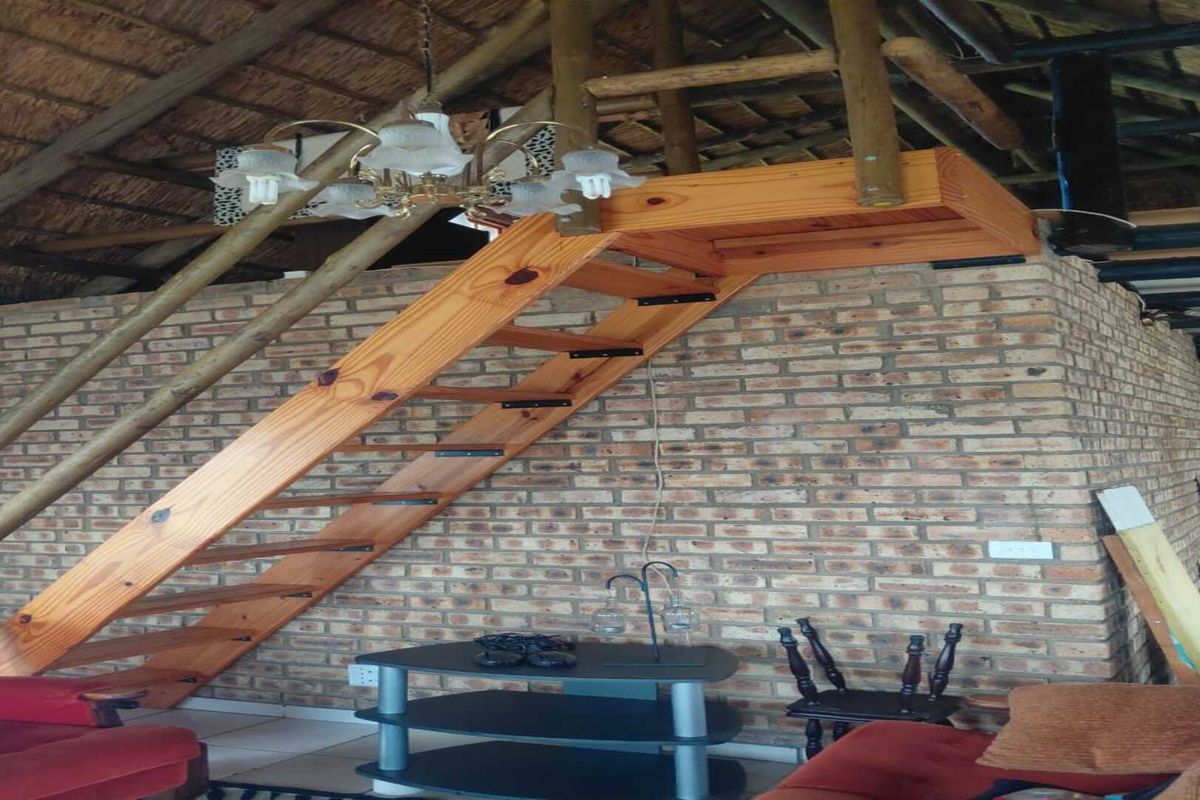 Living area featuring a rustic thatched roof, exposed brickwork, and a wooden staircase leading to a loft level.
