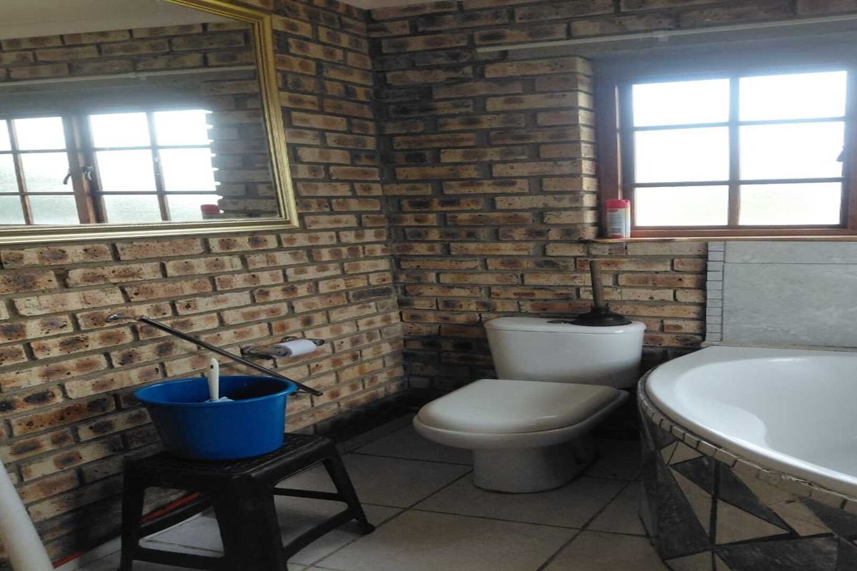 A bathroom featuring a corner bathtub, toilet, and exposed brick walls with a window and mirror.