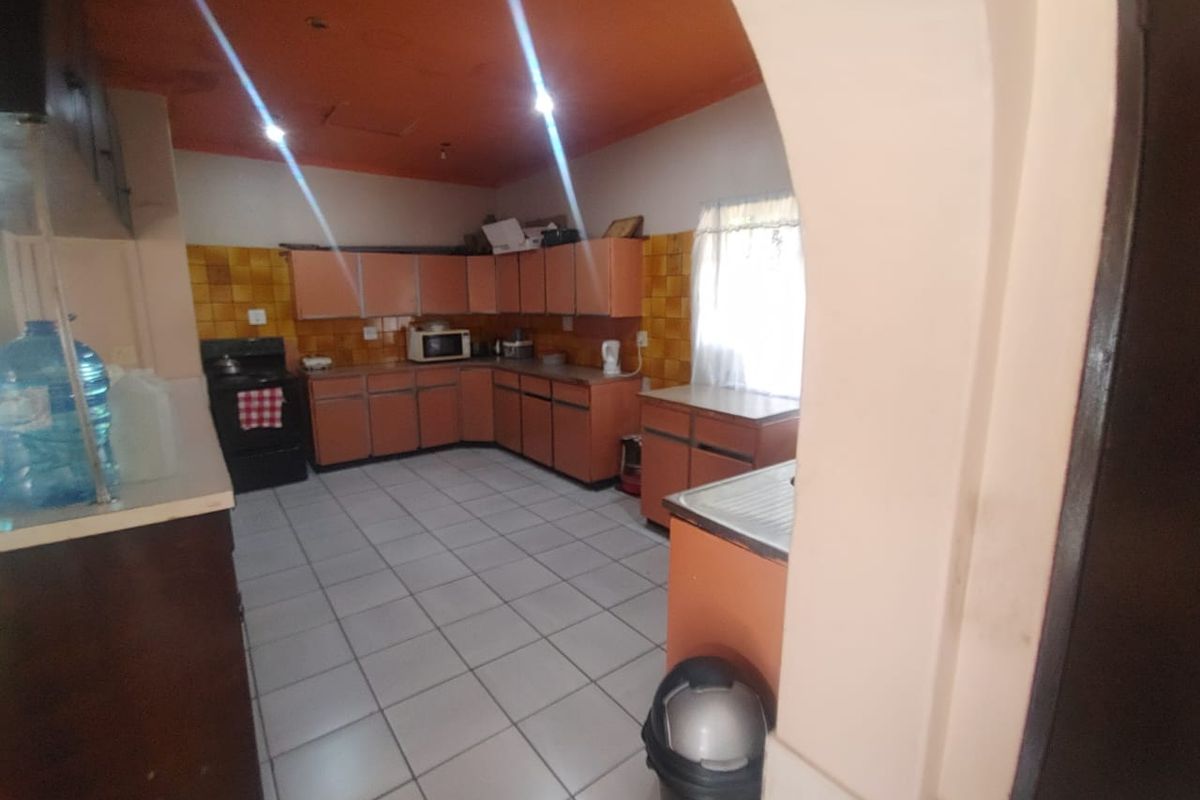 A dated kitchen featuring extensive cabinetry, tiled backsplash, and ceramic floor tiles, viewed through an arched entryway.