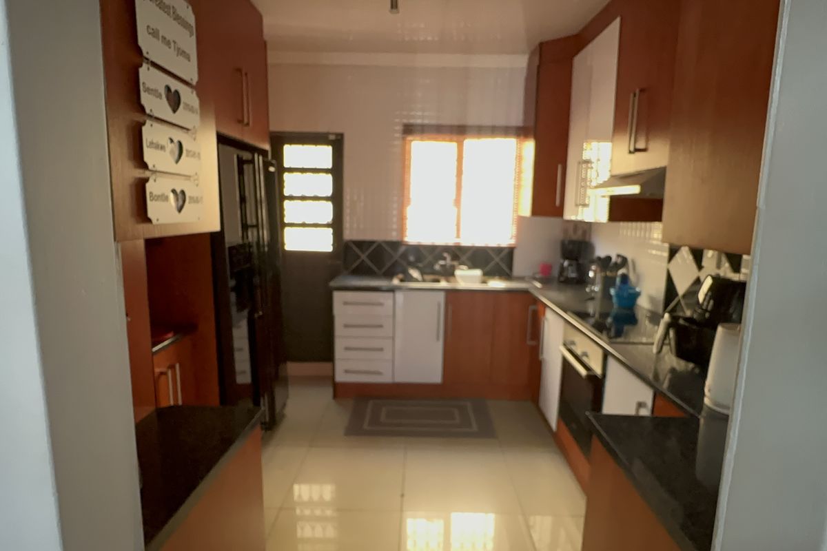 A functional kitchen featuring wooden cabinetry, dark granite countertops, tiled flooring, and a built-in oven with an extractor fan.