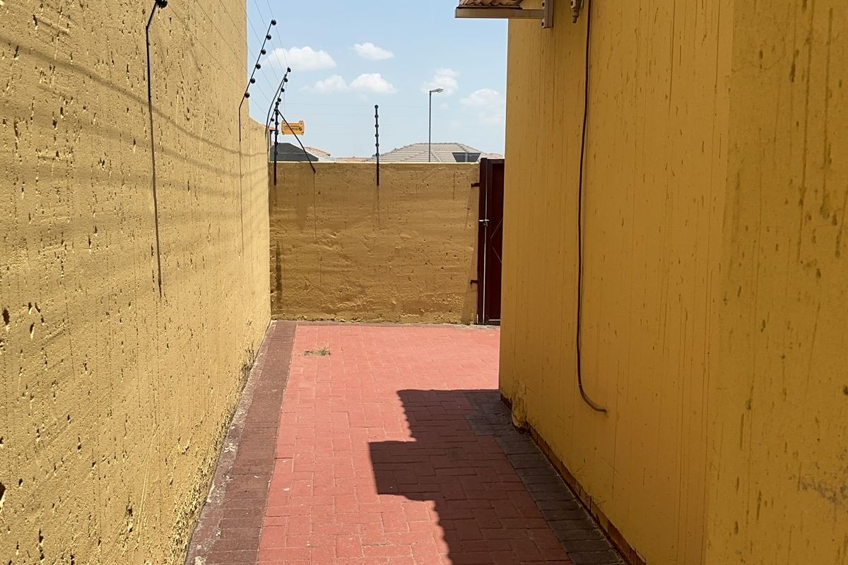 A narrow side passage featuring paved flooring and high perimeter walls with security fencing.