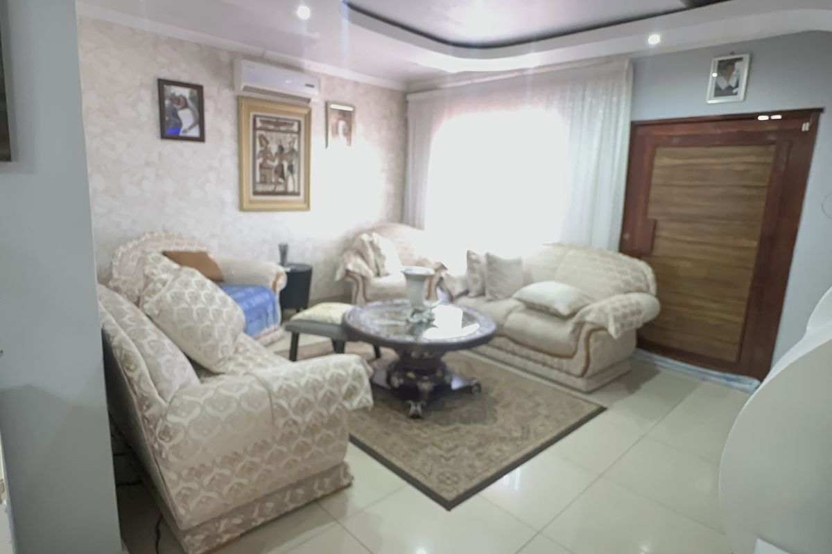A comfortable living room featuring tiled flooring, a tray ceiling with recessed lighting, and a wall-mounted air conditioning unit.