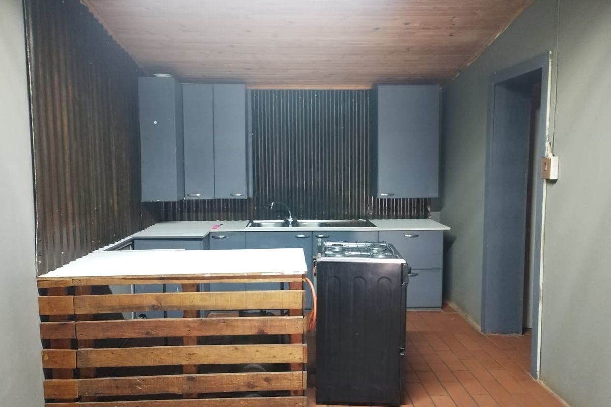A rustic kitchen area featuring dark cabinetry, a stainless steel sink, and a gas stove, set against corrugated metal walls and a timber ceiling.