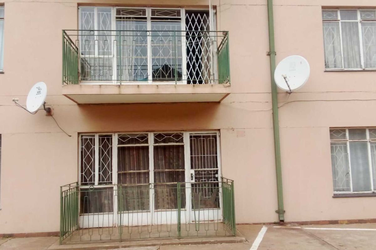 Exterior view of an apartment building featuring two levels of balconies with metal security gates and railings, and satellite dish installations.