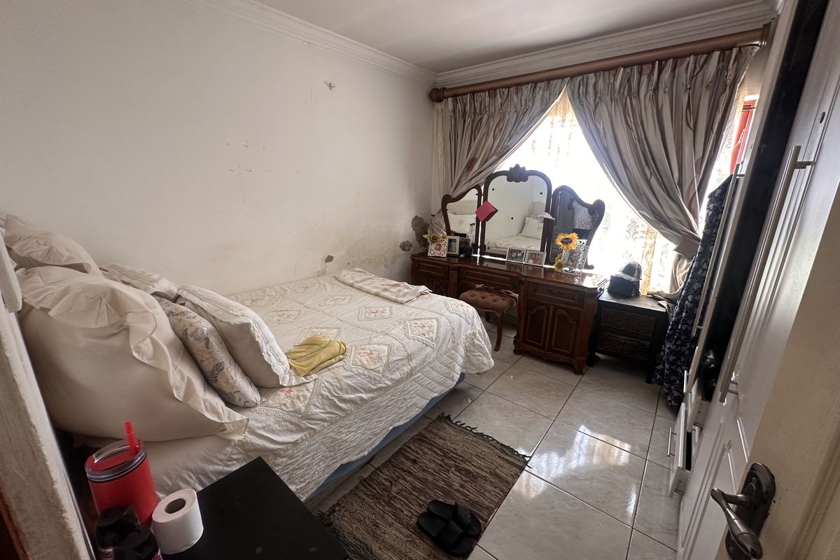 A bedroom featuring tiled flooring and a window with curtain treatments. The walls show visible signs of wear and surface damage.
