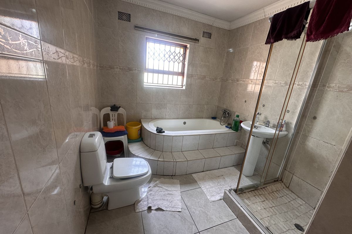 A functional bathroom featuring a built-in bathtub, a separate glass-enclosed shower, a pedestal basin, and a toilet, finished with floor-to-ceiling ceramic wall tiles.