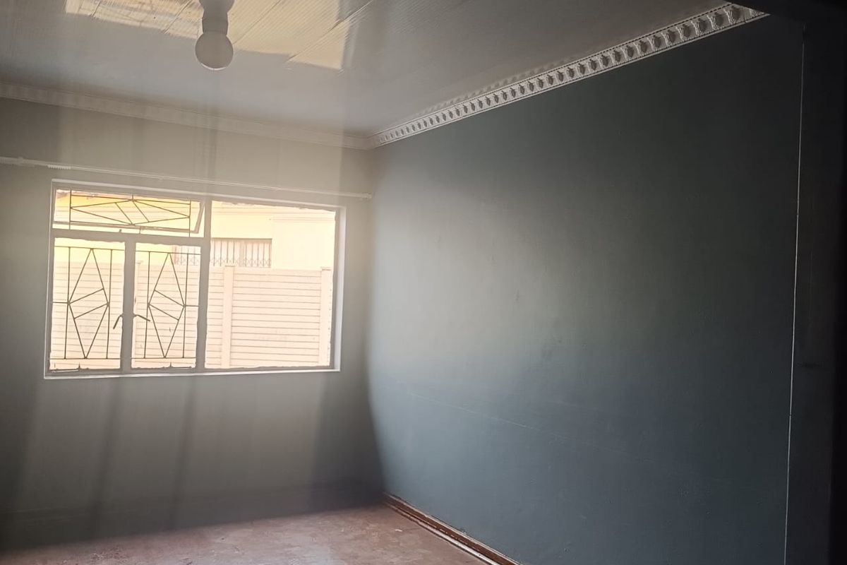 An empty bedroom featuring dark blue walls, a glossy ceiling with decorative cornice, and a window with security bars.