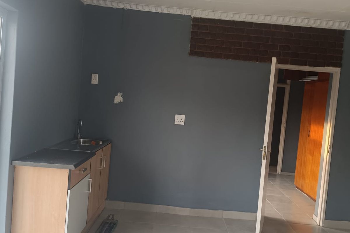 A compact kitchenette area featuring a single base cabinet with a sink, tiled flooring, and decorative ceiling cornicing.