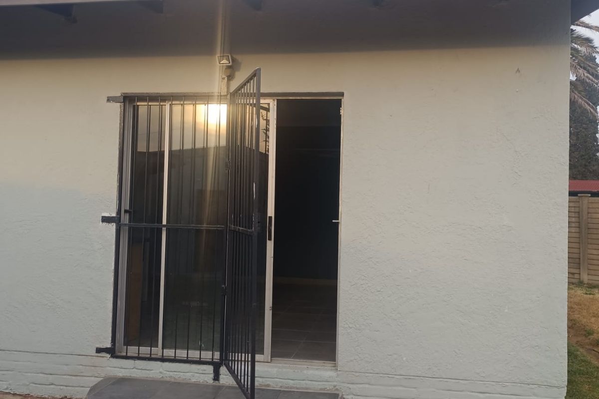 Exterior view of a building featuring a security gate, tiled step, and sliding glass door entrance.