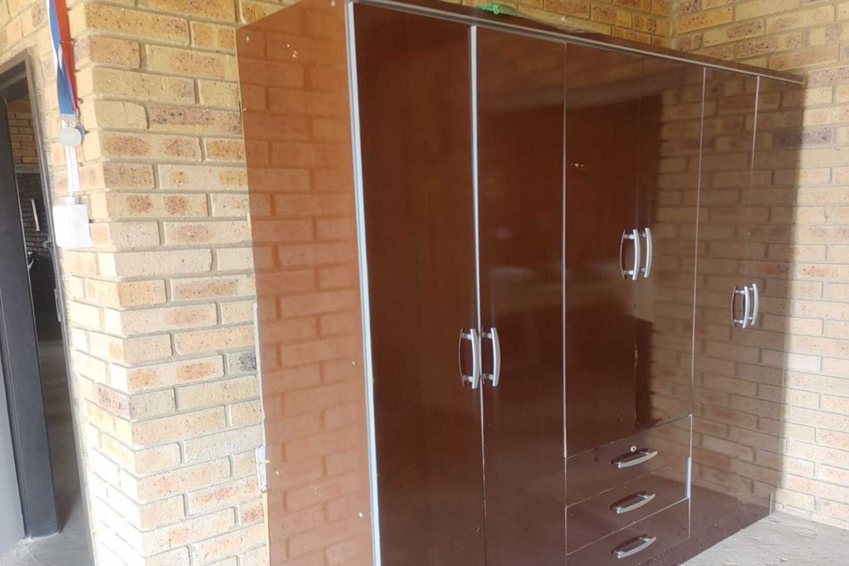 A view of a brick-walled space featuring a large, dark brown built-in wardrobe with multiple doors and drawers.