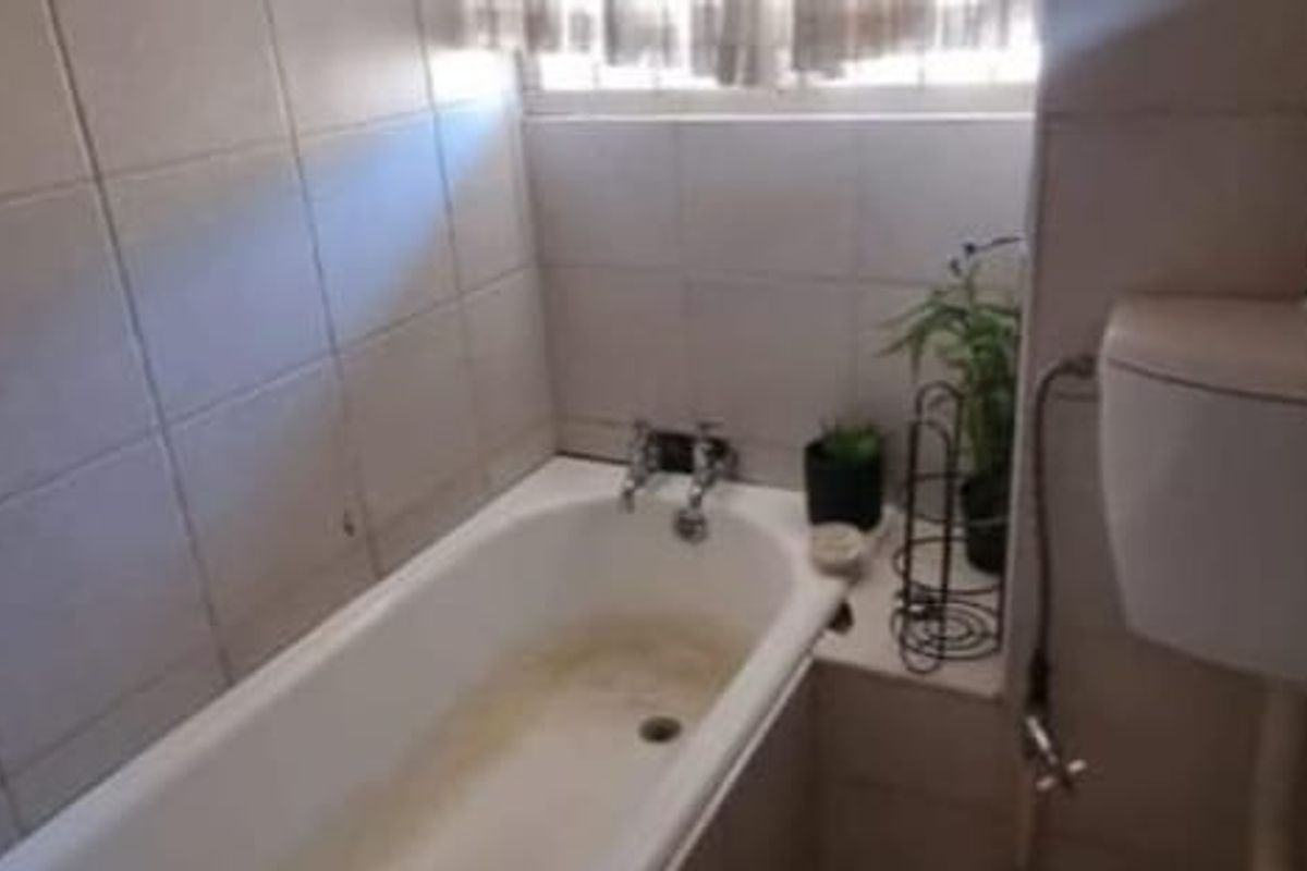 A functional bathroom featuring a standard bathtub with wall-mounted taps and a toilet, finished with neutral wall tiling.