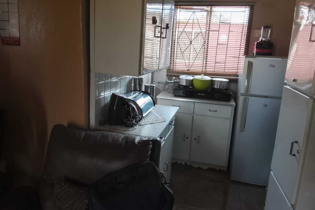 A compact kitchen featuring basic cabinetry, tiled splashbacks, and a window with blinds, offering a functional layout for daily meal preparation.