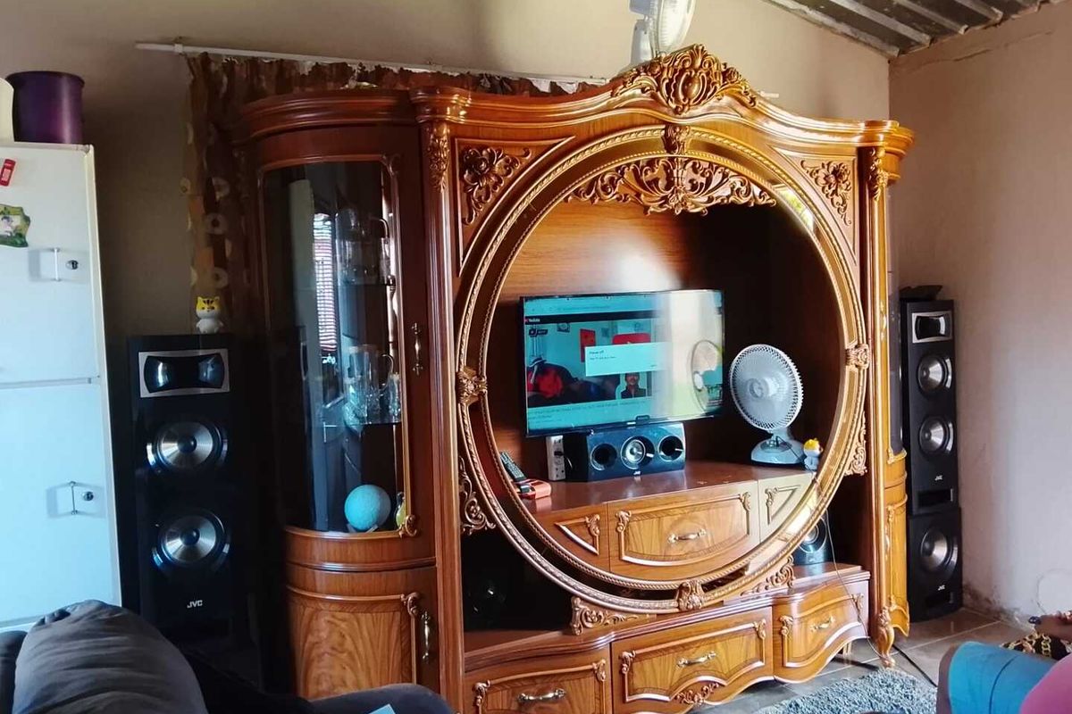 A living room area featuring an ornate wooden entertainment unit and exposed corrugated metal ceiling structure.