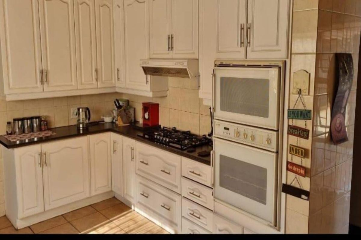 A functional kitchen featuring white cabinetry, a built-in double oven, gas hob, extractor fan, and tiled flooring with a connected scullery area.