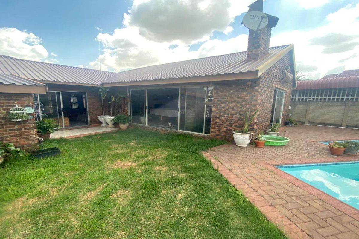 Rear view of the house featuring a brick facade, sliding glass doors, a paved pool deck, and a swimming pool.