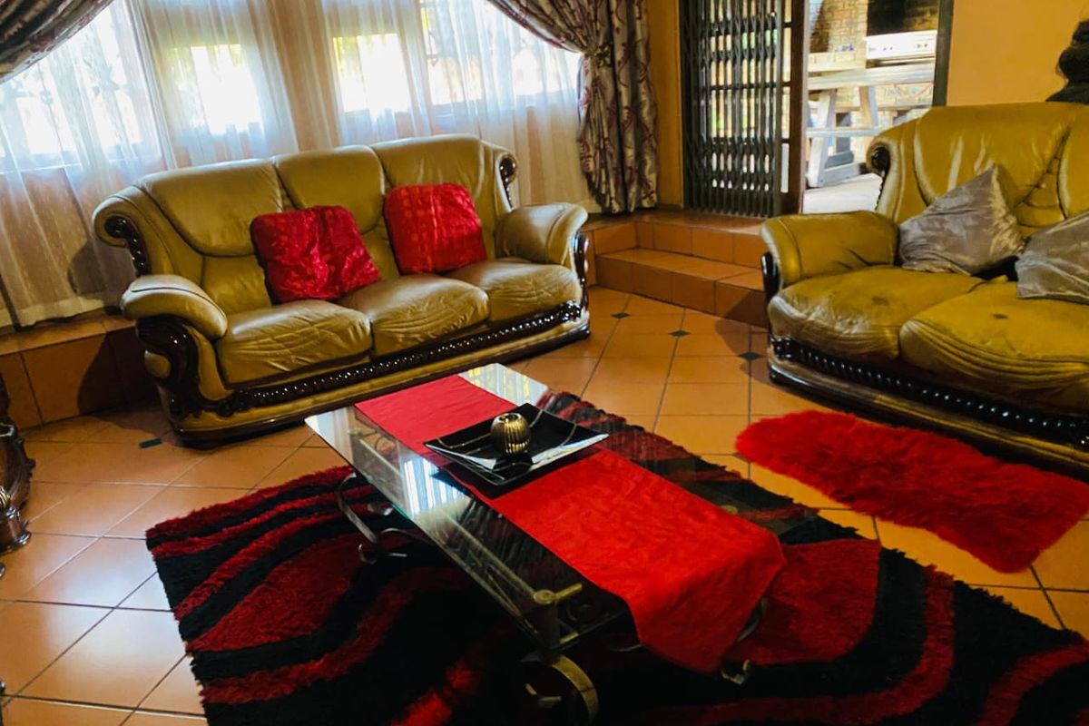 A living room featuring terracotta floor tiles, large windows with curtains, and a step leading to an adjacent outdoor patio area.