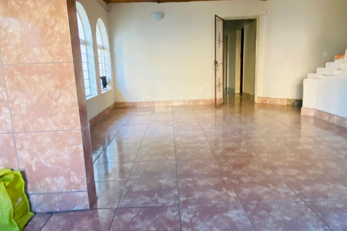 An empty living area featuring tiled flooring, arched windows, and a wooden ceiling, providing a blank canvas for potential renovation.