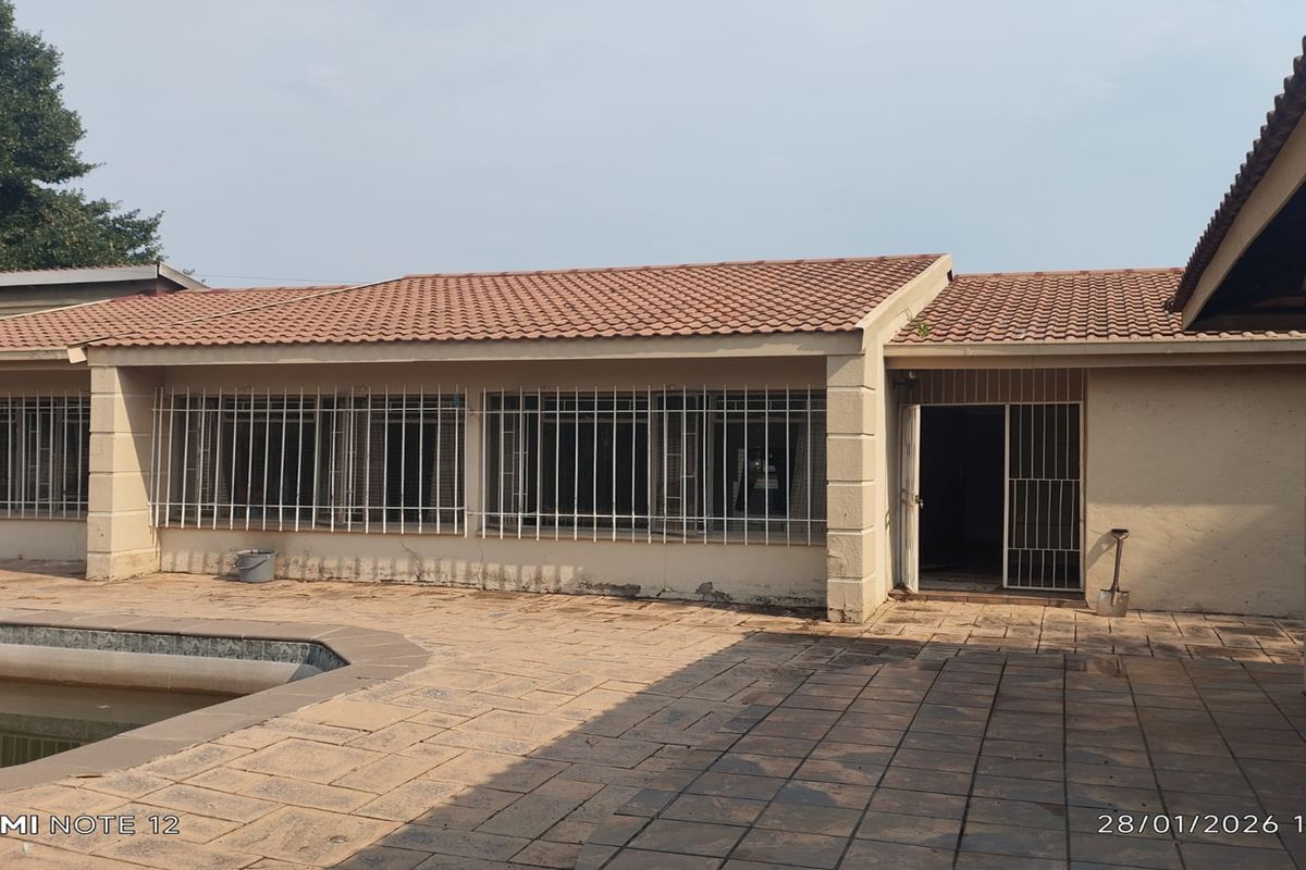 Rear exterior view of the property featuring a tiled patio area, swimming pool, and security bars on windows and doors.