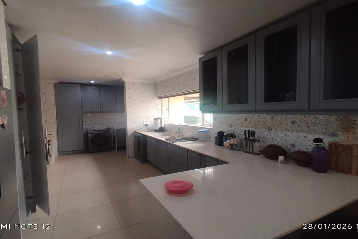Spacious kitchen featuring grey cabinetry, stone countertops, tiled flooring, and integrated laundry area with ample storage and workspace.