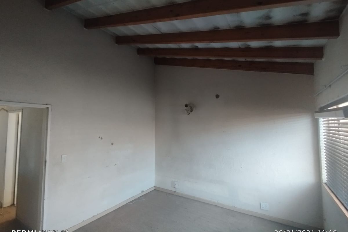 An empty bedroom featuring exposed timber ceiling beams, carpeted flooring, and a window with fitted blinds.