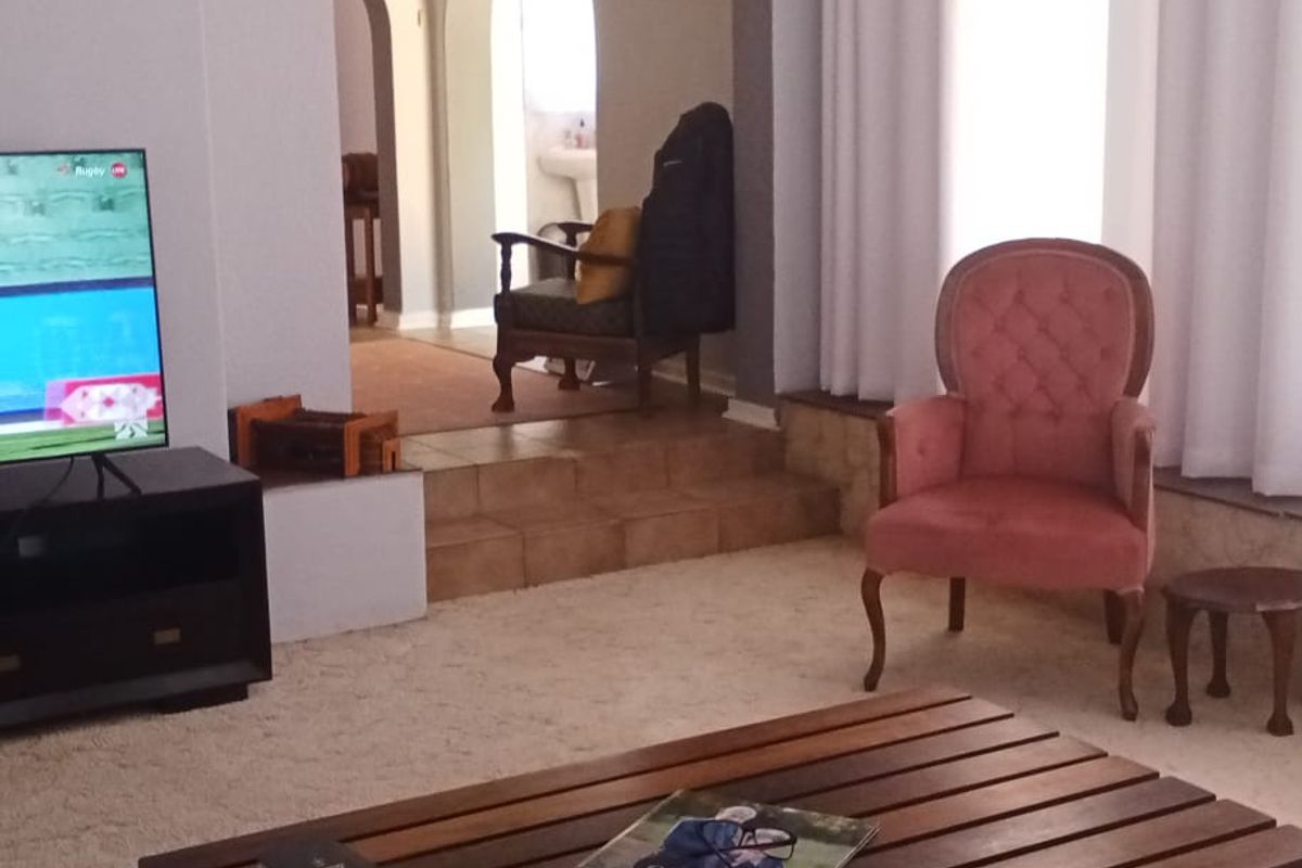 A living room featuring arched doorways leading to an adjacent space, carpeted flooring, and large windows with curtains.