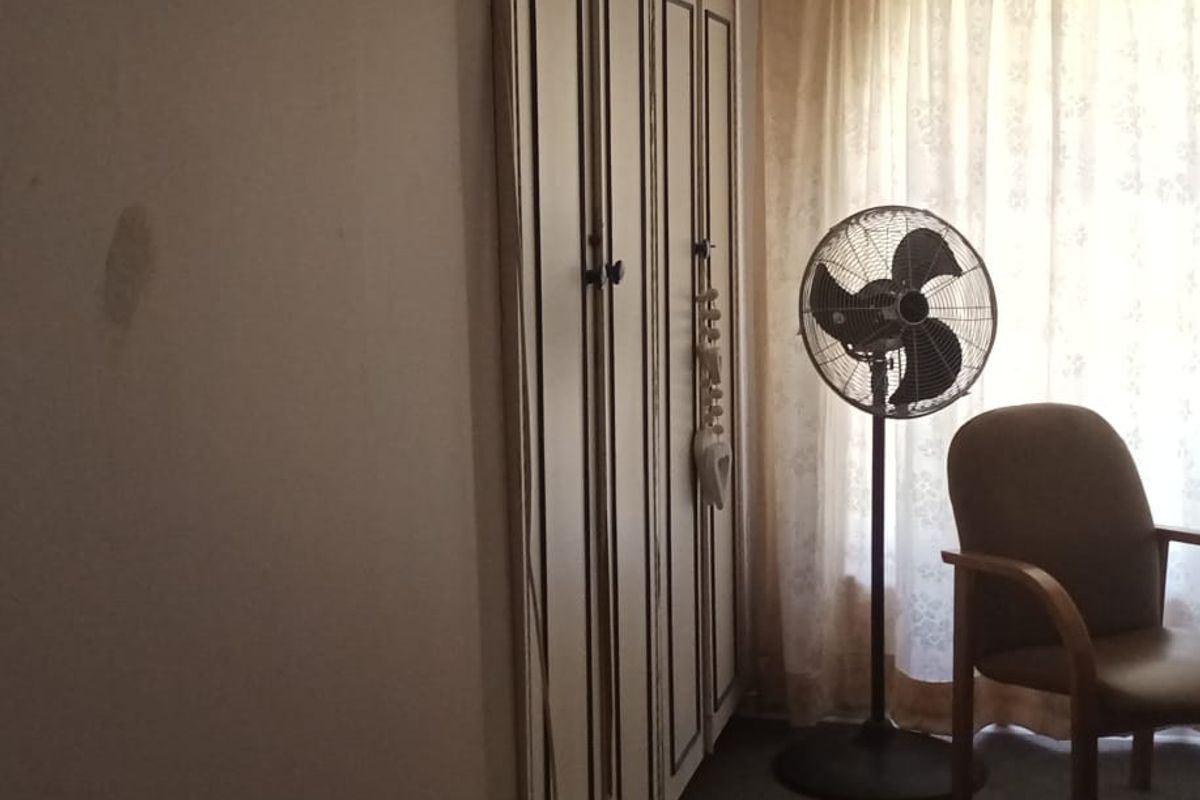 A bedroom featuring built-in cabinetry and a window with curtains, showing signs of wear and requiring cosmetic updates.