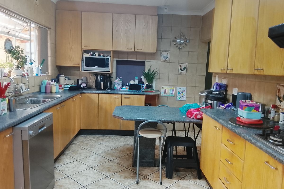 A functional kitchen featuring wooden cabinetry, tiled splashbacks, a built-in hob, and a breakfast nook area with tiled flooring.
