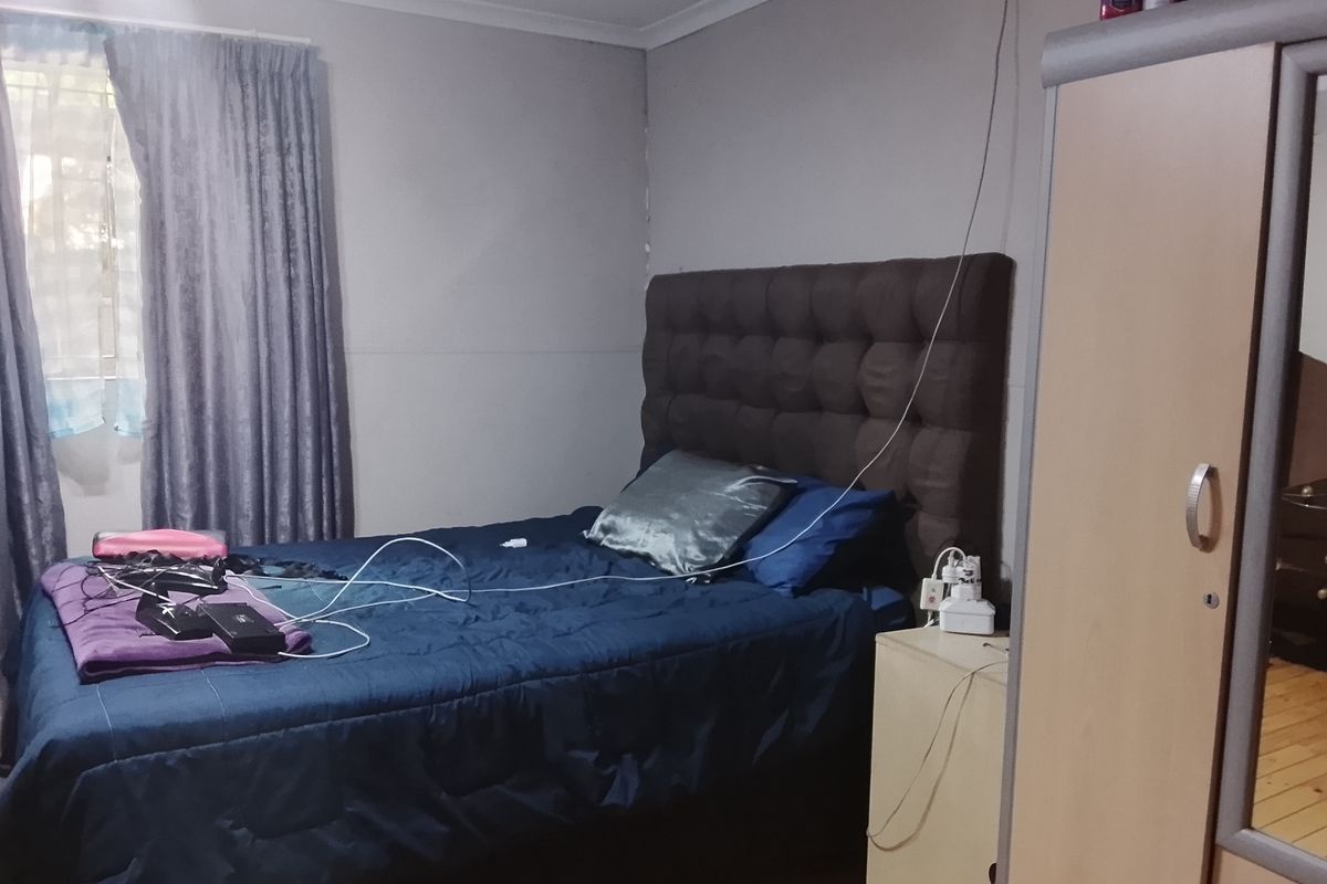 A functional bedroom featuring timber flooring, a window with curtain treatments, and built-in wardrobe space.