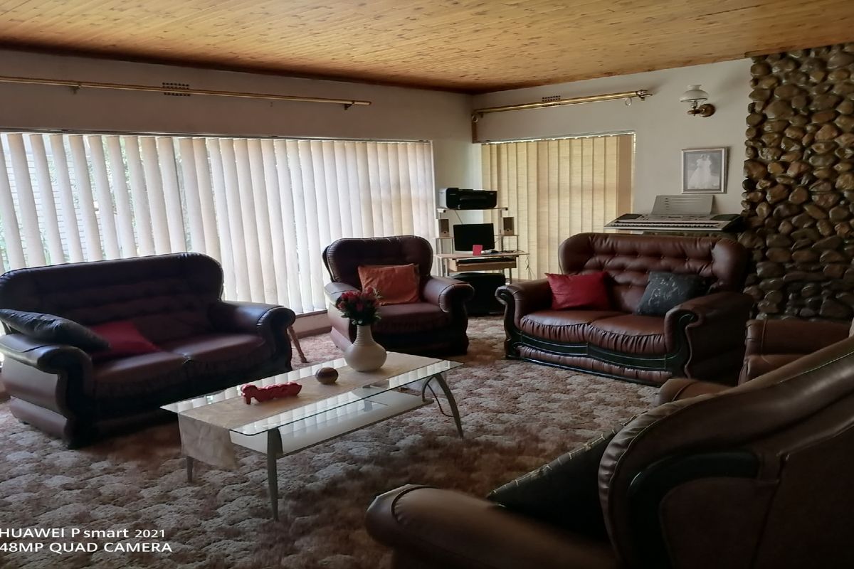 Spacious living room featuring a prominent stone-clad fireplace, timber-paneled ceiling, and large windows with vertical blinds.
