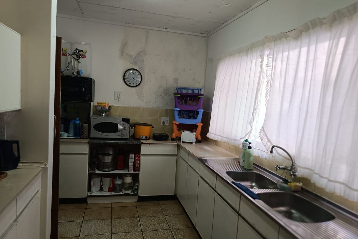A dated kitchen featuring a double stainless steel sink, tiled splashbacks, and original cabinetry, requiring significant renovation and repair to the walls and ceiling.