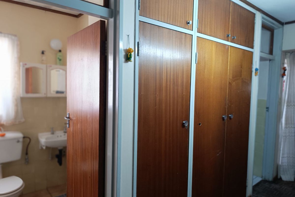 A bedroom featuring built-in wooden cupboards with an adjacent view into a functional bathroom with a toilet and wall-mounted basin.