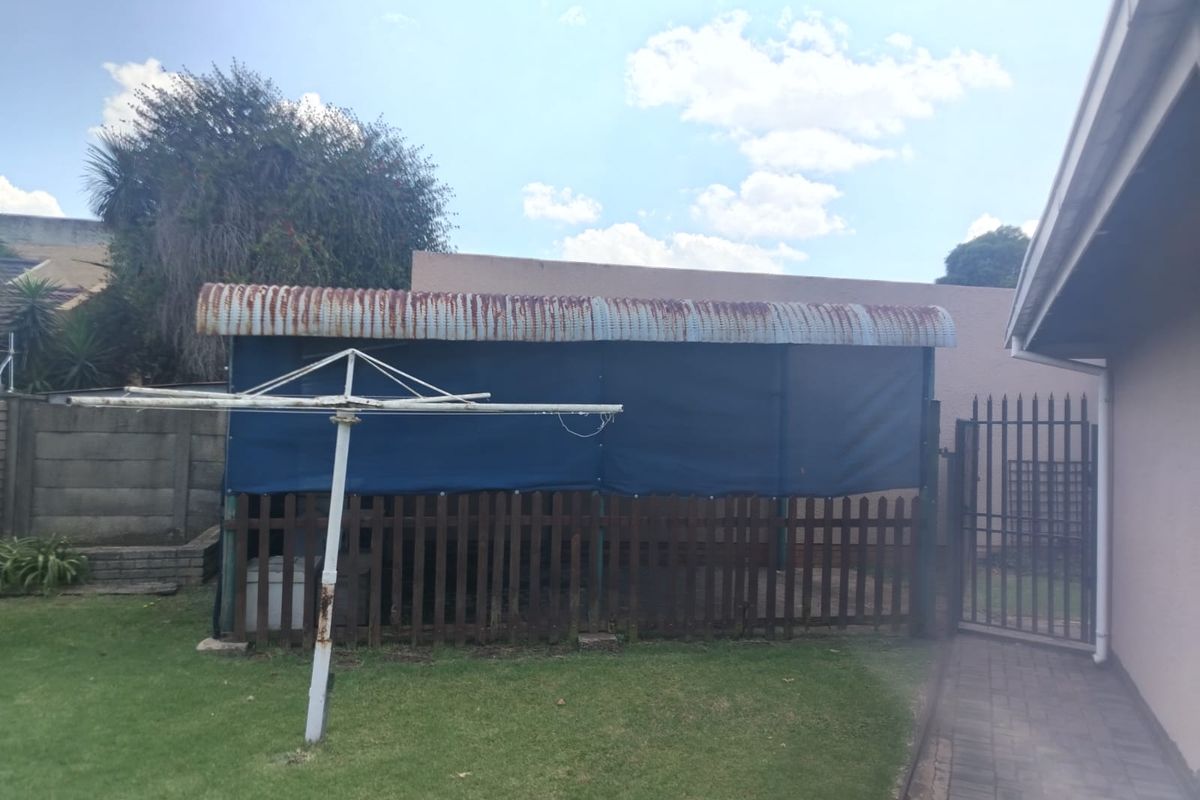 Rear garden area featuring a lawn, paved walkway, metal security gate, and a covered outdoor structure with a rusted corrugated roof.