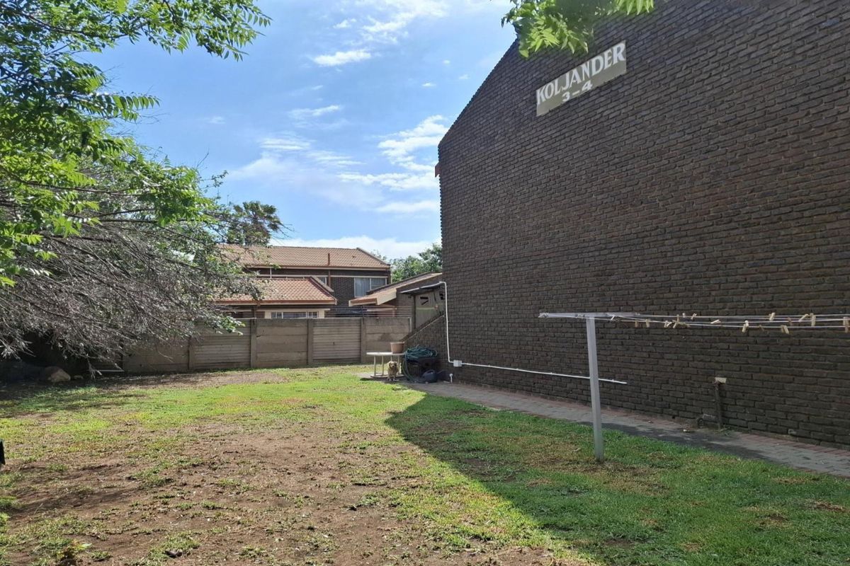 A view of the rear garden area featuring a brick townhouse facade, perimeter walling, and a paved walkway along the building exterior.