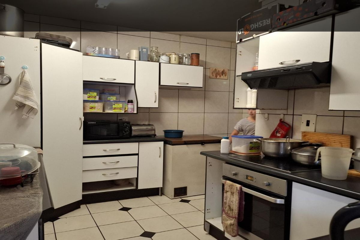 A functional kitchen featuring built-in cabinetry, a fitted oven, hob, and extractor fan with tiled walls and flooring.