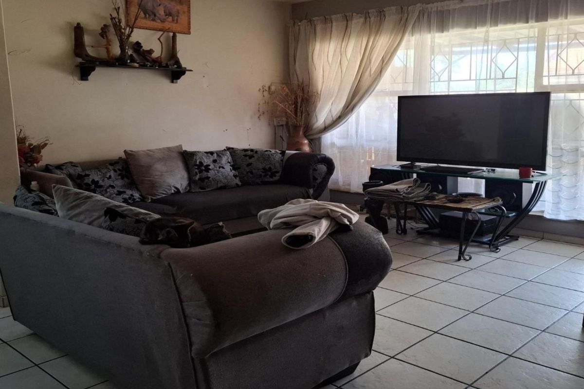 A spacious living room featuring large windows with security bars and tiled flooring, offering a functional layout for comfortable family living.