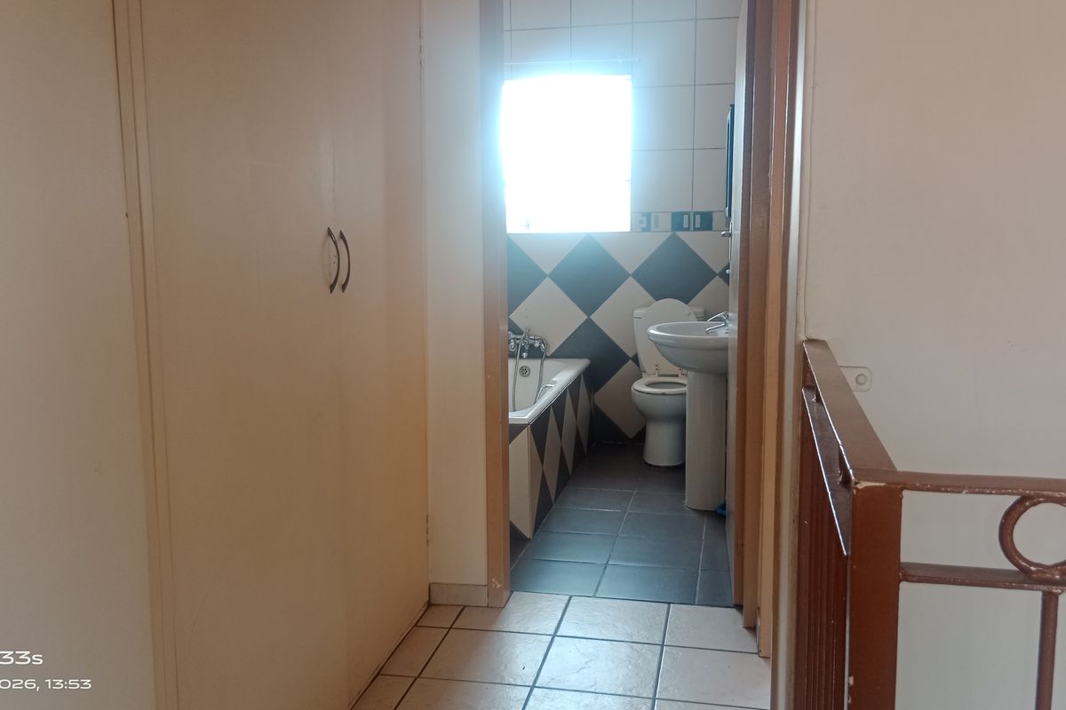 A view from the hallway into a bathroom featuring a bathtub, pedestal basin, and toilet with a diamond-patterned tiled splashback.