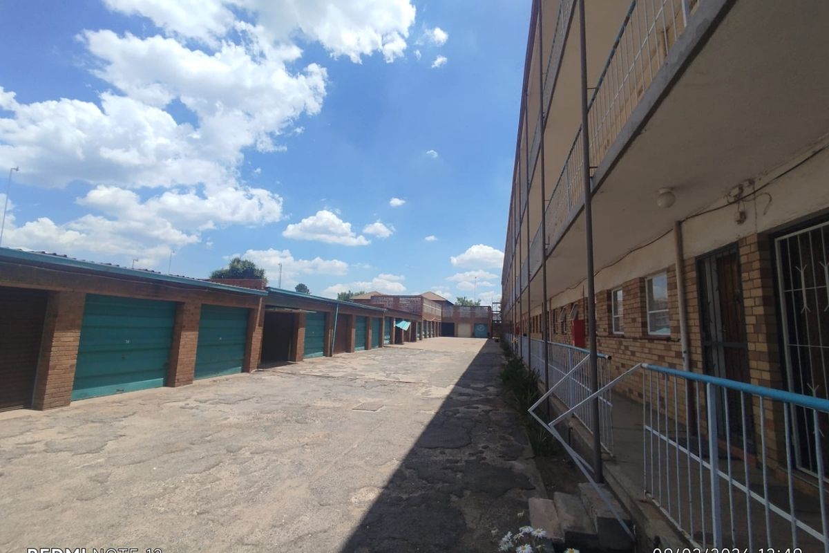 Exterior view of an apartment complex featuring a row of garages and a multi-story building with external walkways and metal railings.
