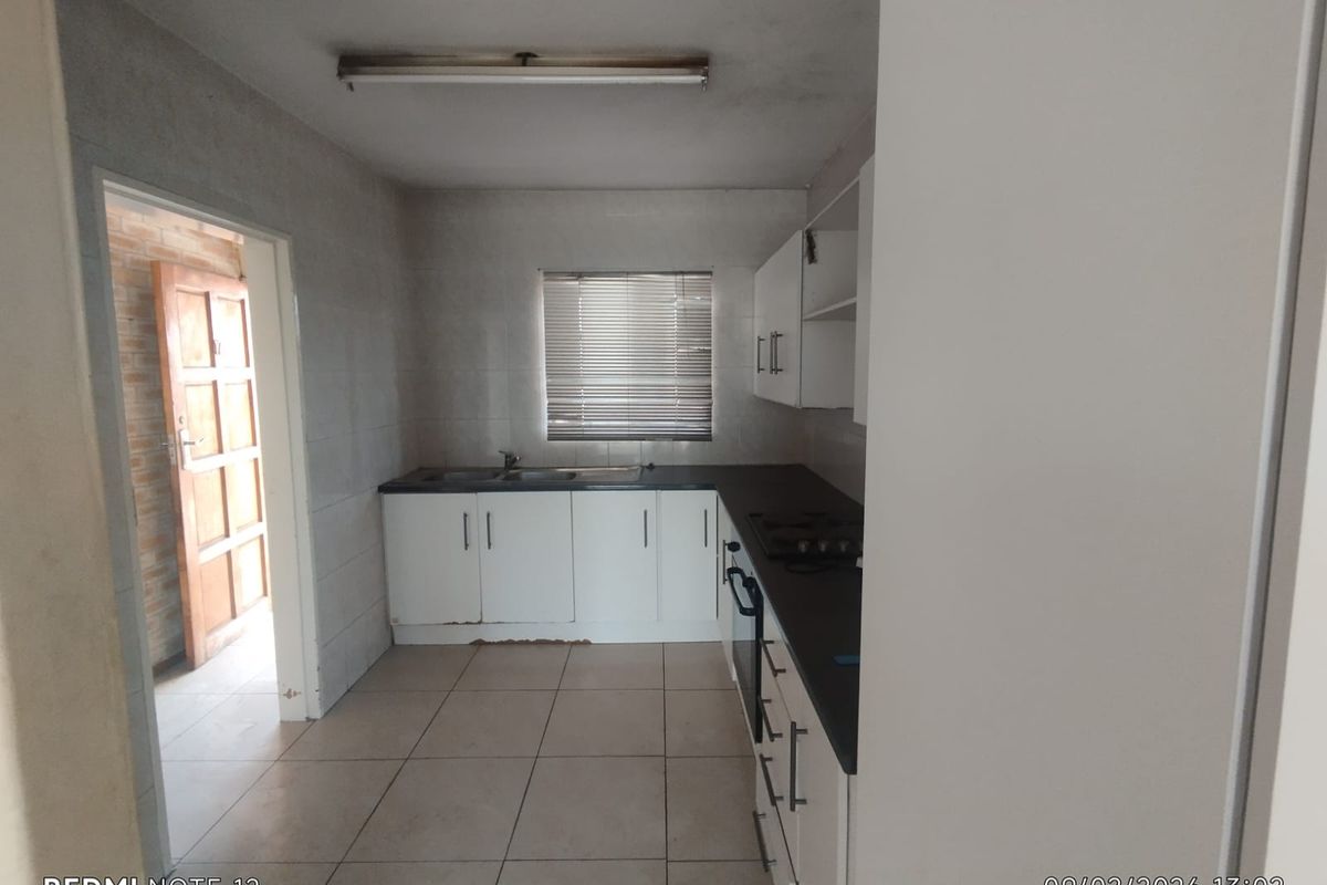 A functional kitchen featuring white cabinetry, dark countertops, tiled flooring, and a window with blinds, providing a practical workspace in need of cosmetic updates.