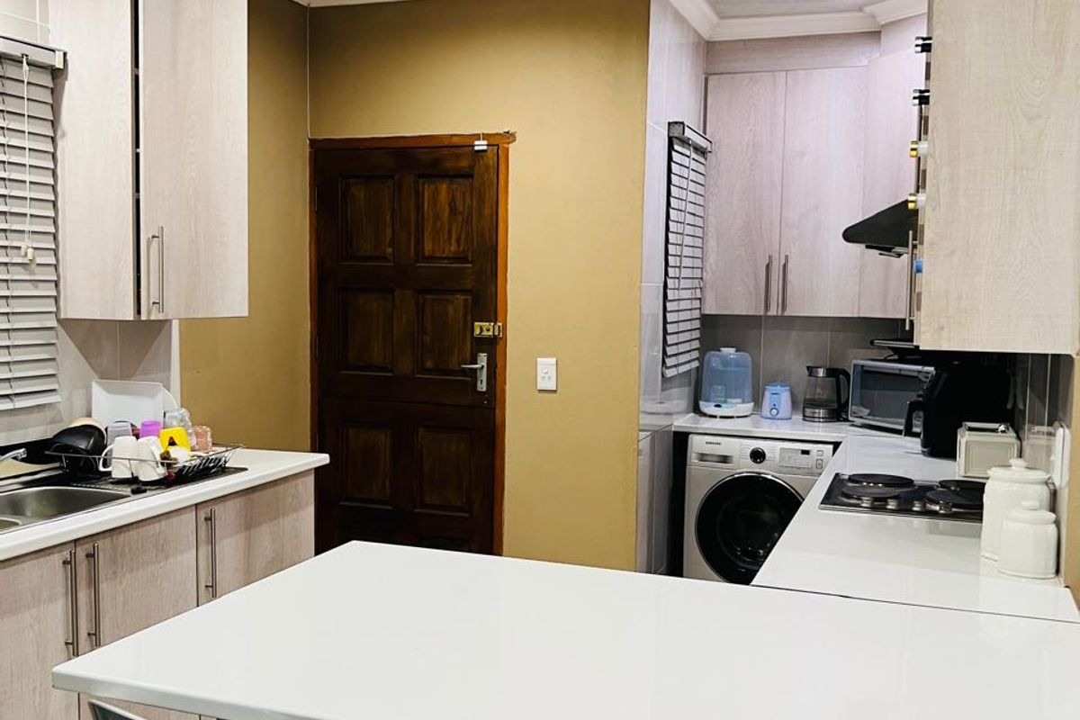 A functional kitchen featuring light wood-look cabinetry, white countertops, a breakfast bar, and integrated laundry space with a built-in washing machine.