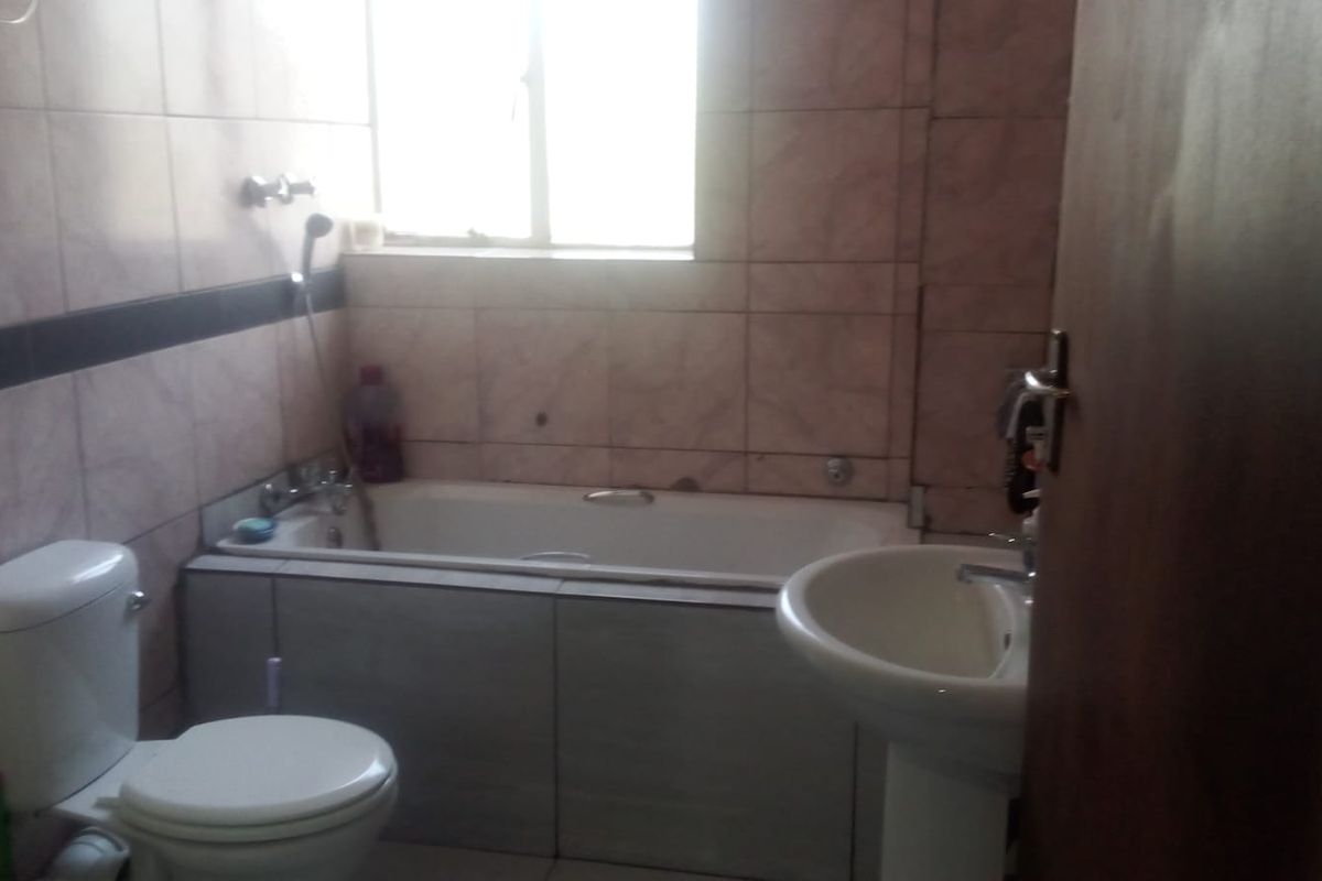 A functional bathroom featuring a bathtub, pedestal basin, and toilet with tiled walls and flooring.