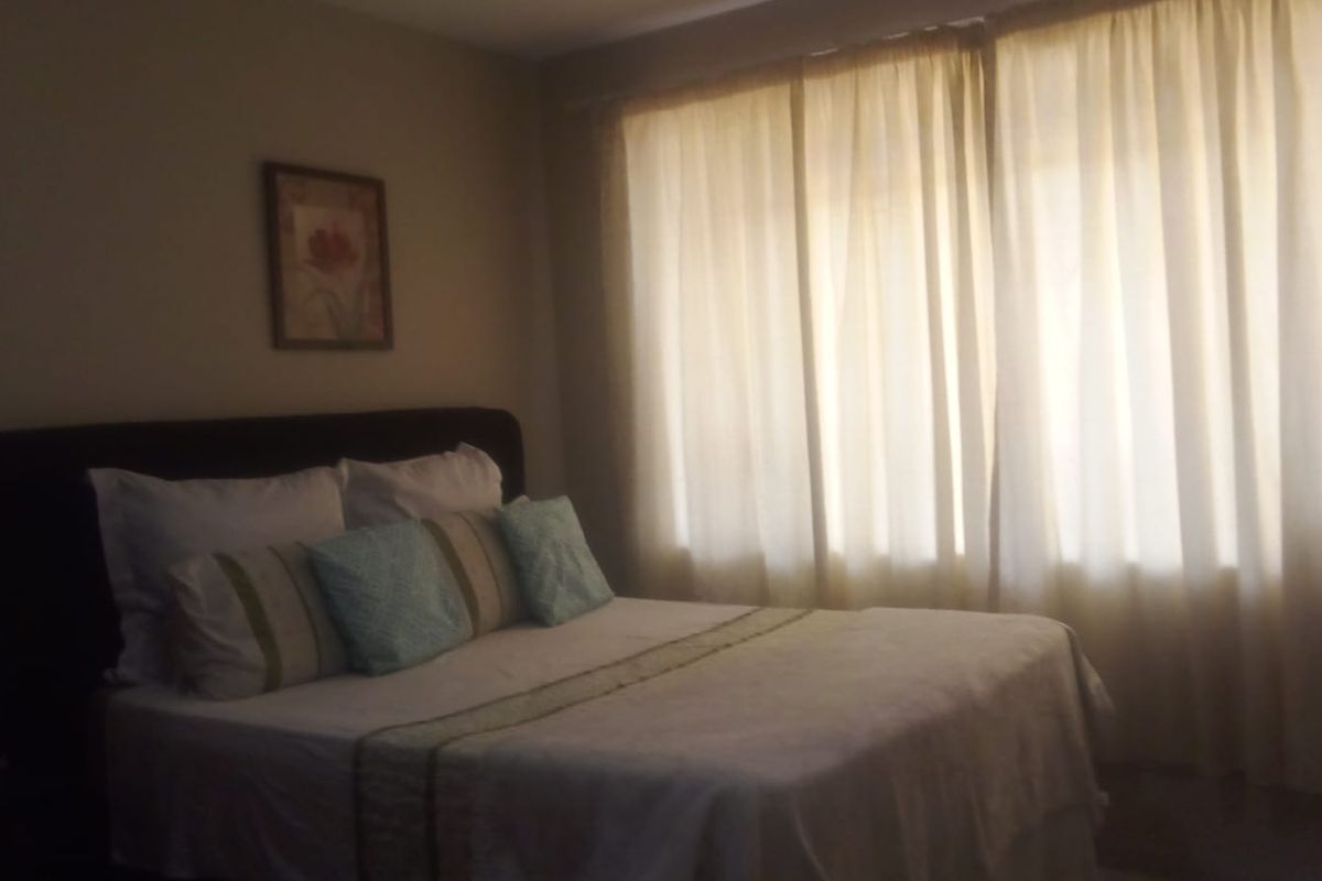 A bedroom featuring neutral wall tones and large windows covered by curtains, providing natural light to the space.